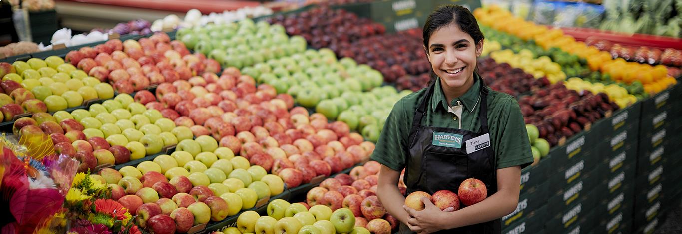Harveys Supermarket Produce Associate working in the Produce Department holding some fresh fruit and smiling.
