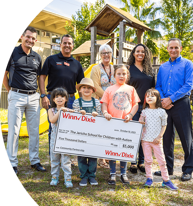 Group of Southeastern Grocers associates standing next to teachers from The Jericho School for Children with Autism. In front of them are young students holding a big $5,000 check.