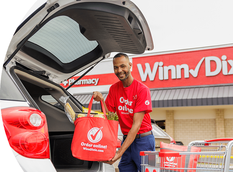 Winn-Dixie associate placing a produce-filled reusable Winn-Dixie bag in the back of a car trunk.