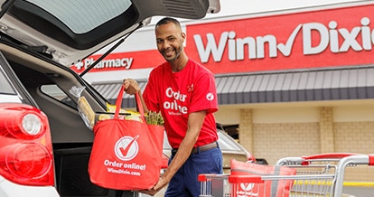 Winn-Dixie associate placing a produce-filled reusable Winn-Dixie bag in the back of a car trunk.