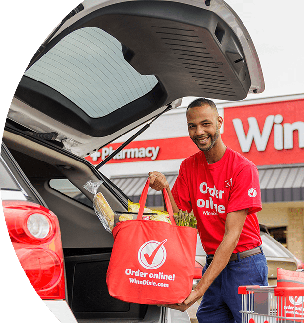 Winn-Dixie associate placing a produce-filled reusable Winn-Dixie bag in the back of a car trunk.