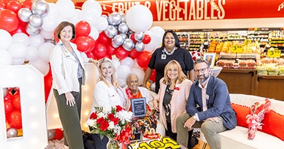 Various members of different organizations standing and sitting next to Romay Davis. They are all joyfully smiling. In front of the group there is a cake with the number '104'.