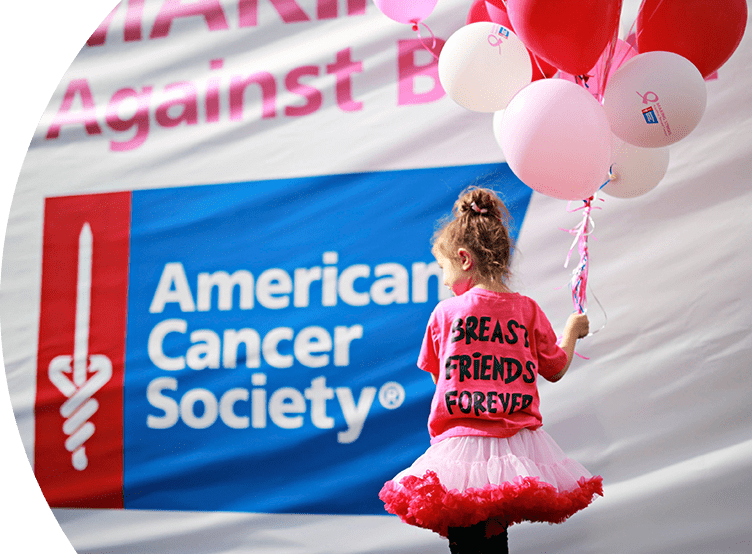 Young girl holding pink balloons. She is wearing a pink tutu and a pink shirt that says "Breast Friends Forever". Behind her there is the American Cancer Society® logo placed on a banner.