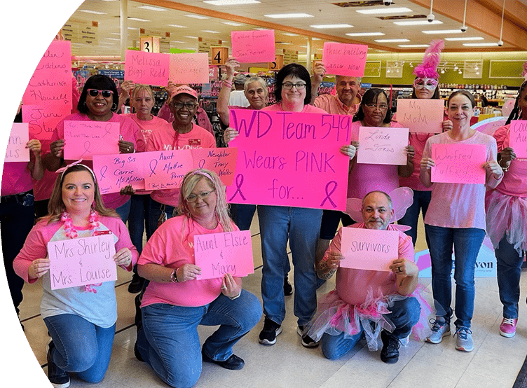 Group of WInn-Dixie associates and Breast Cancer Awareness supporters wearing pink shirts and holding up pink signs with the names of Breast Cancer patients and survivors.