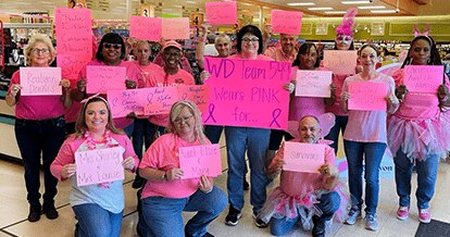 Group of WInn-Dixie associates and Breast Cancer Awareness supporters wearing pink shirts and holding up pink signs with the names of Breast Cancer patients and survivors.