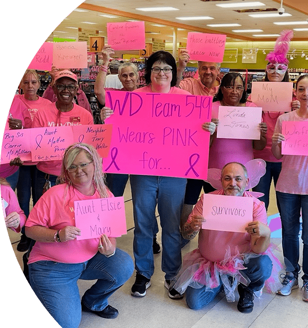 Group of WInn-Dixie associates and Breast Cancer Awareness supporters wearing pink shirts and holding up pink signs with the names of Breast Cancer patients and survivors.