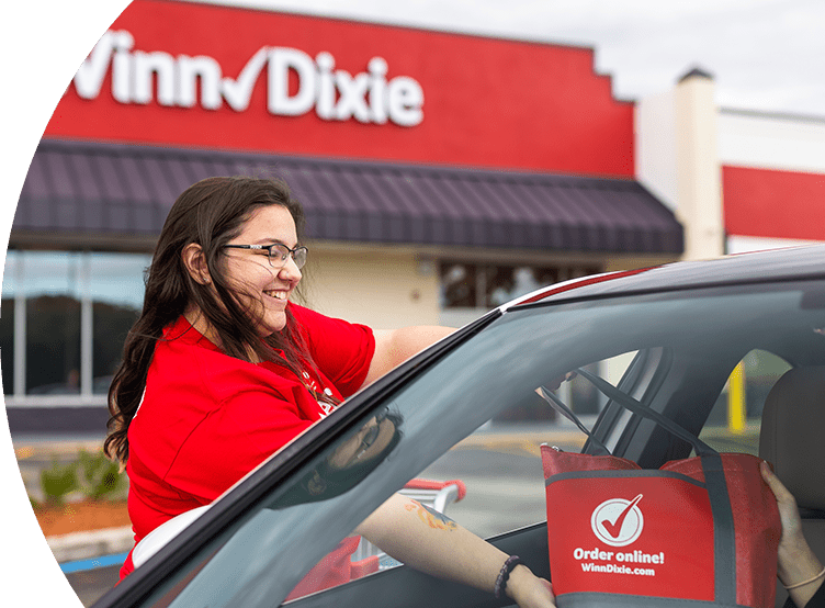 Winn-Dixie associate handing a grocery-filled bag to a customer inside their car.