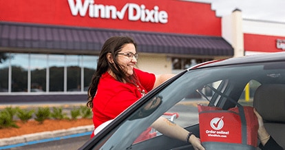 Winn-Dixie associate handing a grocery-filled bag to a customer inside their car.