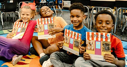 Kids smiling in a classroom holding books