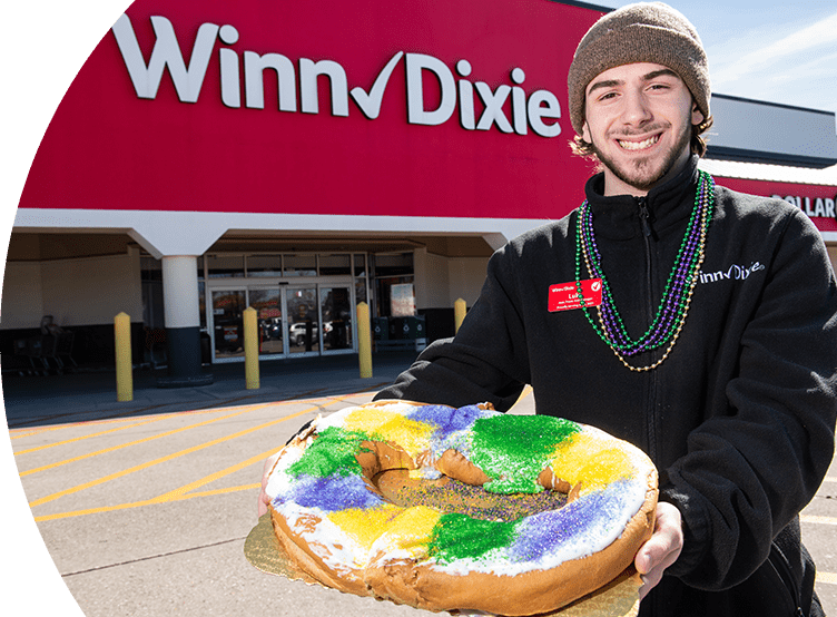 Male Winn-Dixie employee smiling holding a king cake outside of a store