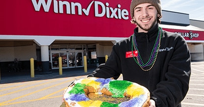 Male Winn-Dixie employee smiling holding a king cake outside of a store