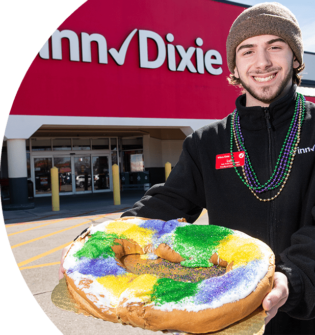 Male Winn-Dixie employee smiling holding a king cake outside of a store