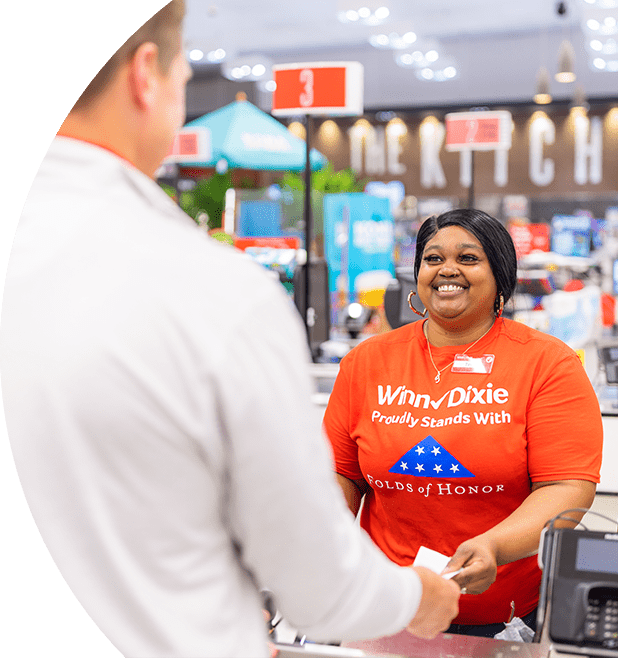 Smiling Winn-Dixie cashier wearing a Folds of Honor shirt. On the foreground, a customer is making a transaction.