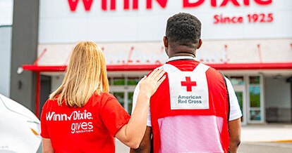 Winn-Dixie female employee with hand on male American Red Cross volunteer's shoulder. Looking towards the outside of a Winn-Dixie.