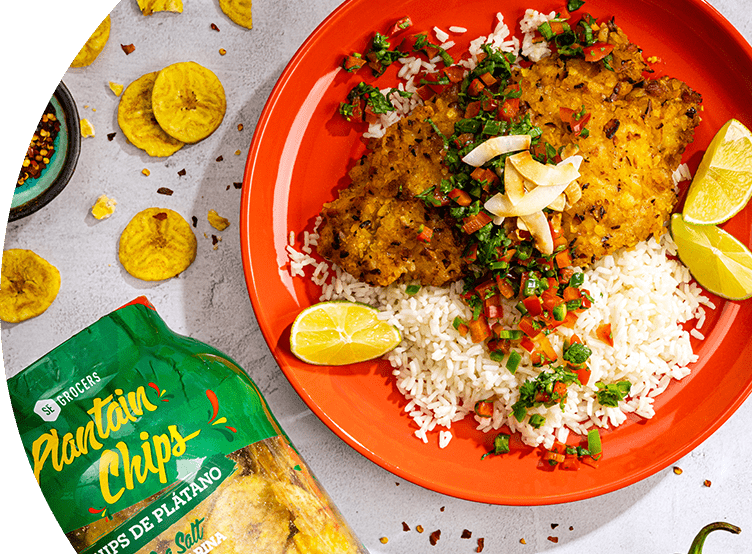 Plantain-crusted cod with coconut rice served on a plate. Next to the plate, there is a container of SE Grocers plantain chips.