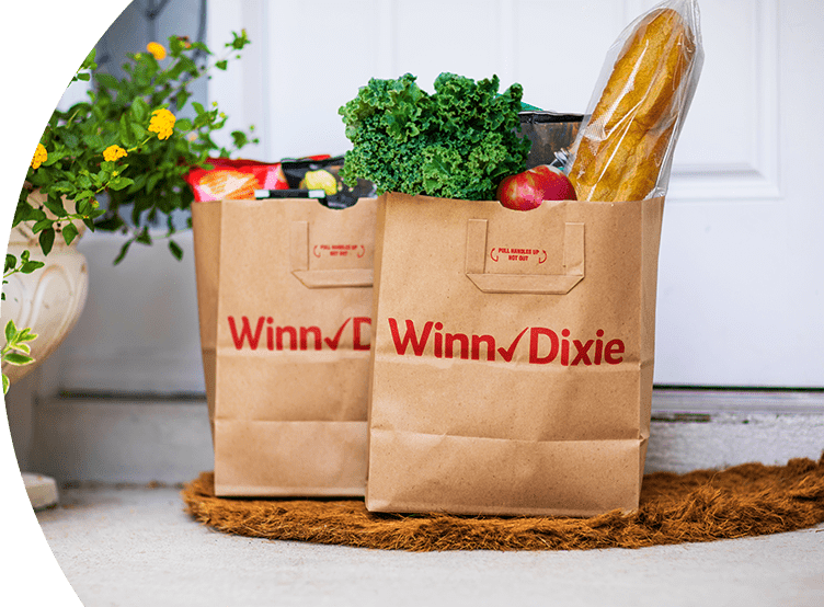 Two produce-filled Winn-Dixie paper bags sitting on a doorstep