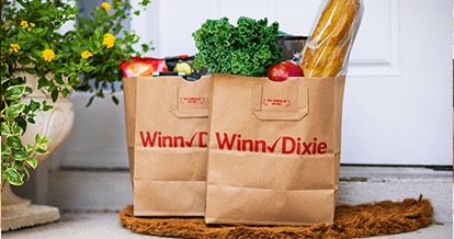 Two produce-filled Winn-Dixie paper bags sitting on a doorstep