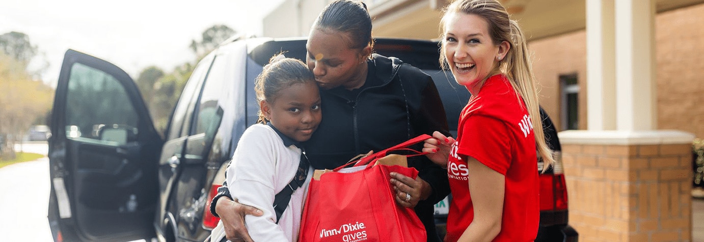 Gives Foundation volunteer handing Winn-Dixie bag to mom and daughter.