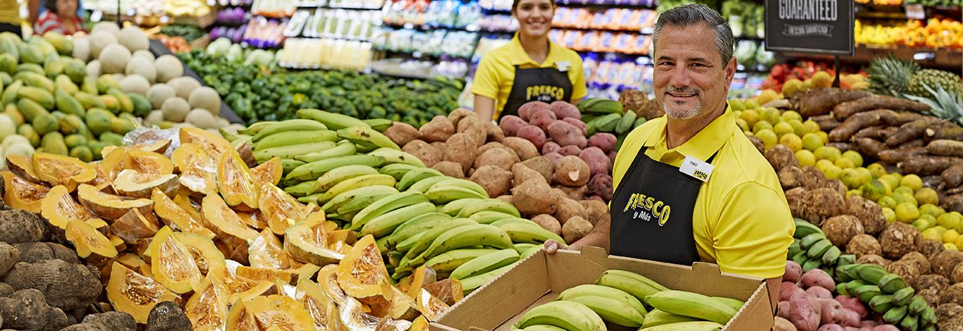 Fresco y Más Produce Associate smiling while restocking fresh produce.